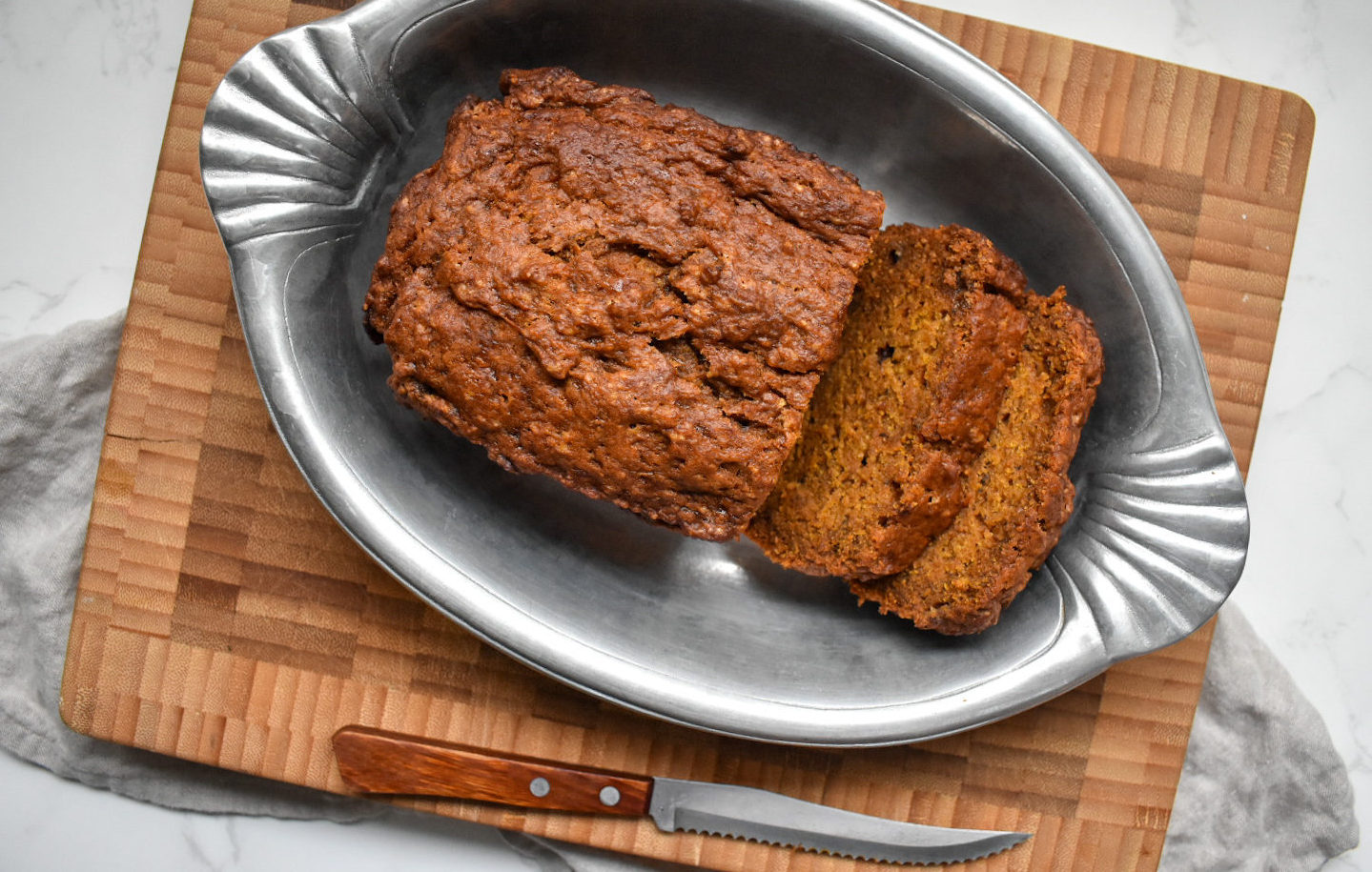 Sliced pumpkin banana bread sits in a pan, on a cutting board.