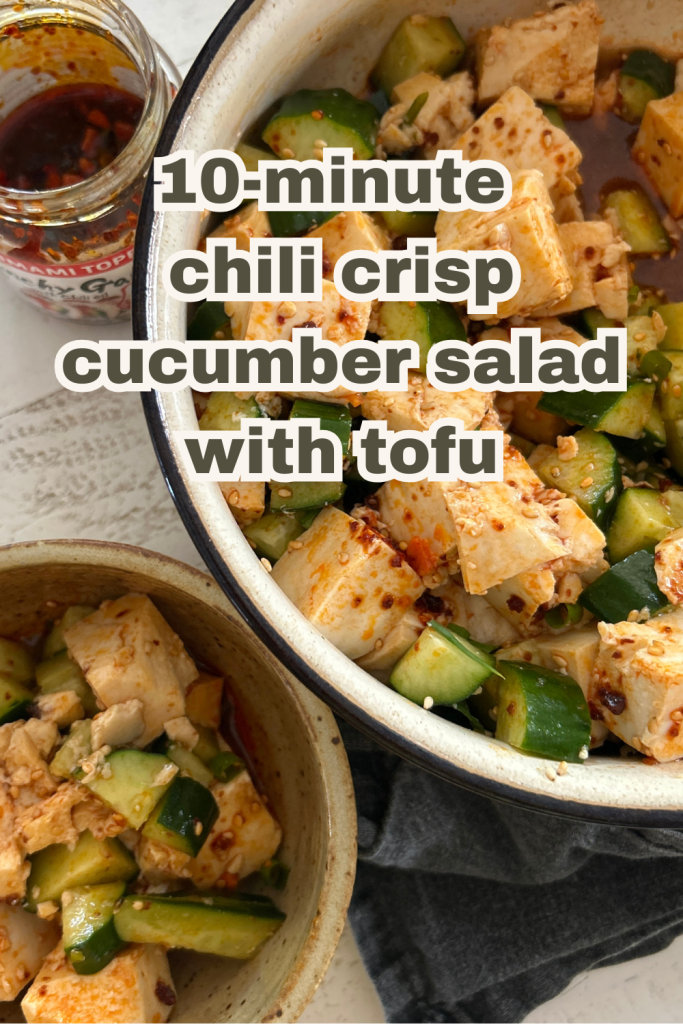 An easy spicy, Asian-style cucumber salad recipe with soft tofu, cucumbers, chili crisp/chili crunch, sesame seeds in a large bowl. A jar of chili crunch is off to the side.